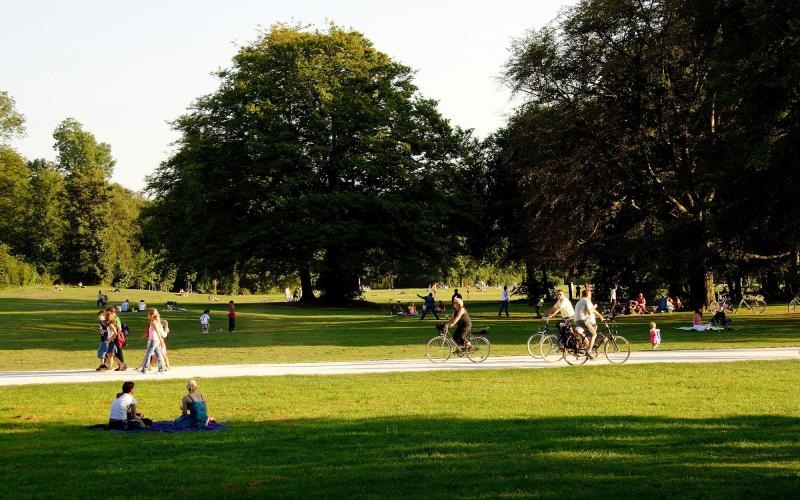 A park with many people riding bikes, having a picnic, and walking.